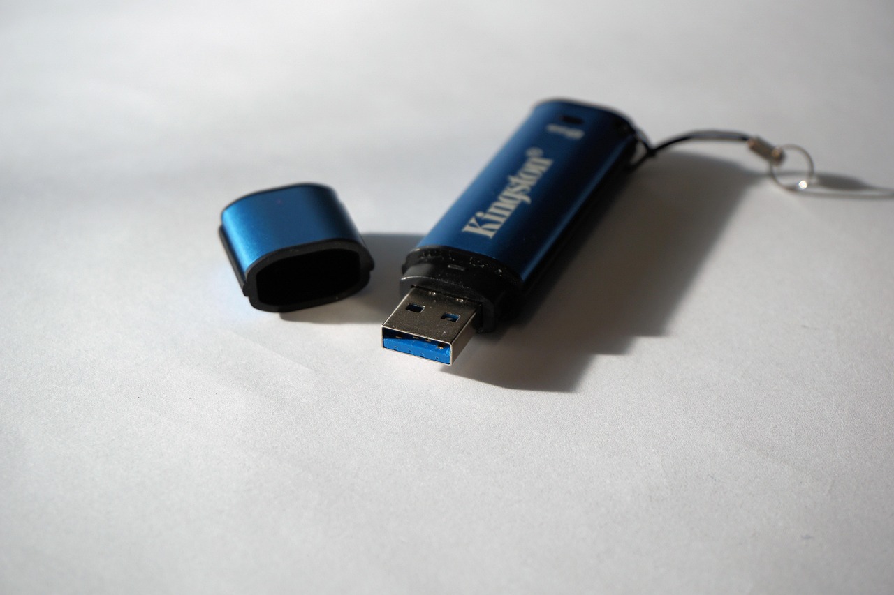 A blue Kingston USB flash drive with its cap removed, lying on a plain white surface next to its lanyard